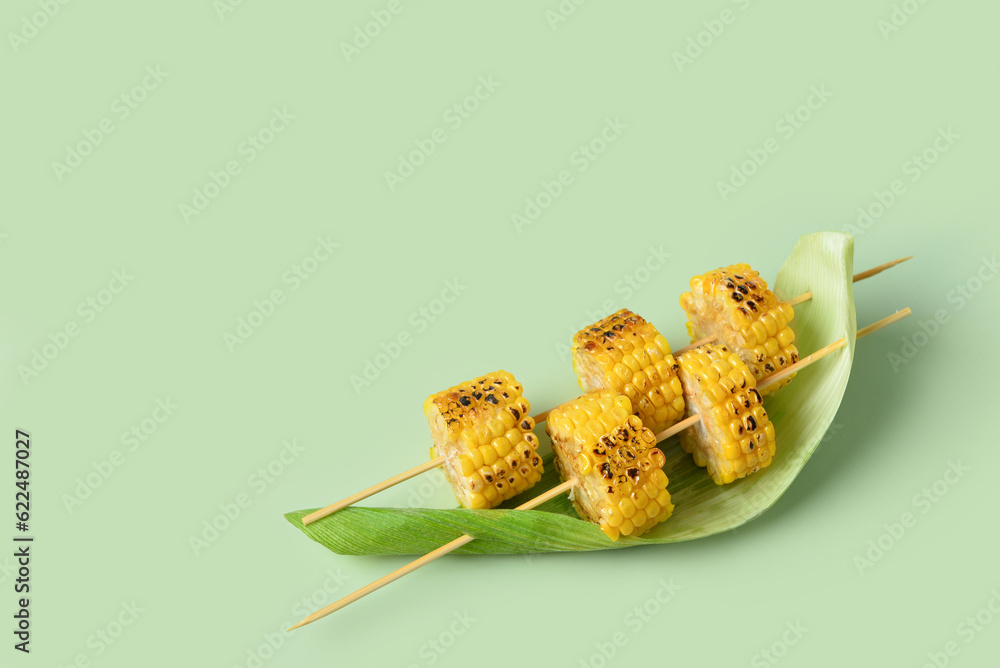 Tasty grilled corn cob skewers on green background