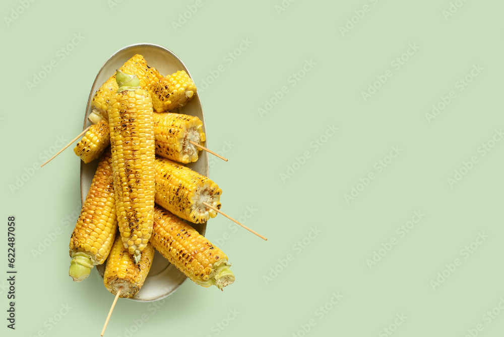 Bowl with tasty grilled corn cobs on green background