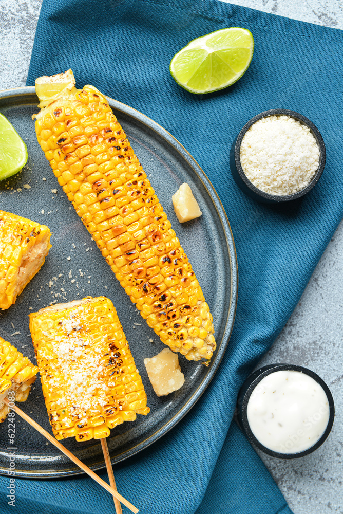 Plate with tasty grilled corn cob skewers and cheese on blue background