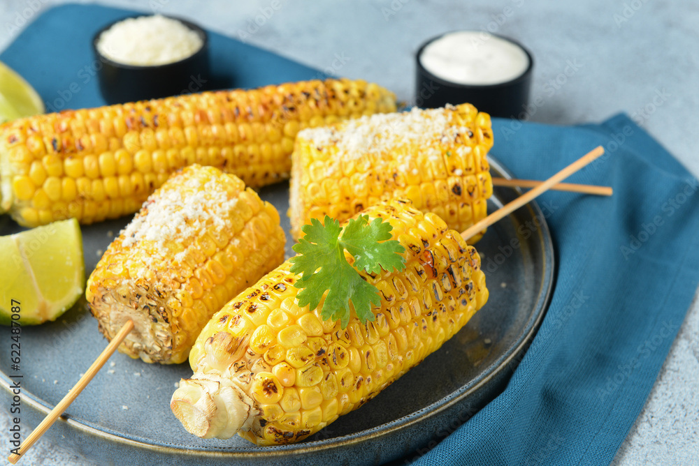 Plate with tasty grilled corn cob skewers and cheese on blue background