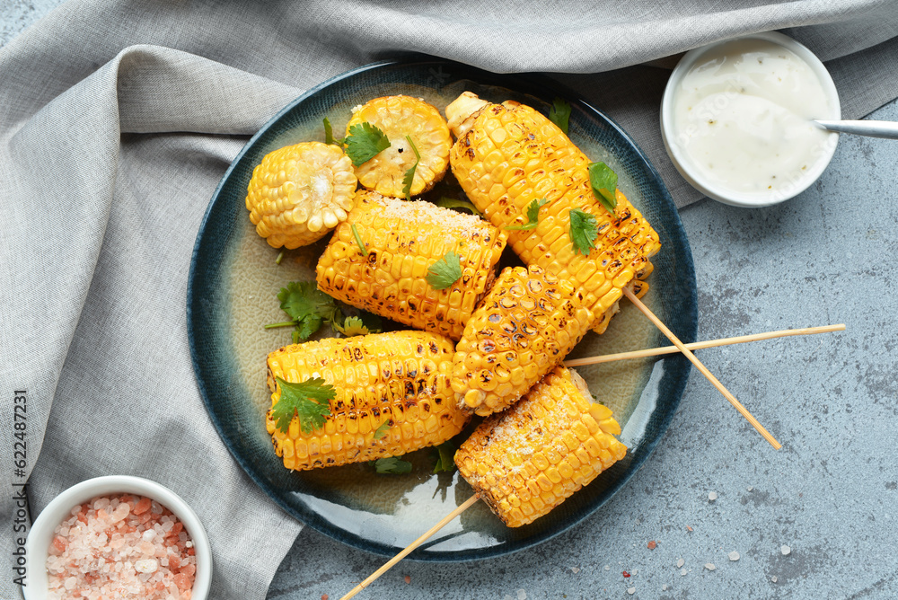 Plate with tasty grilled corn cob skewers and parsley on blue background