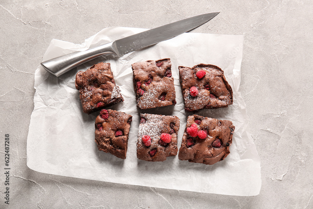 Baking paper with pieces of raspberry chocolate brownie on grey table