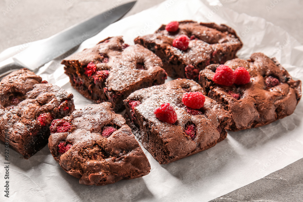 Baking paper with pieces of raspberry chocolate brownie on grey table