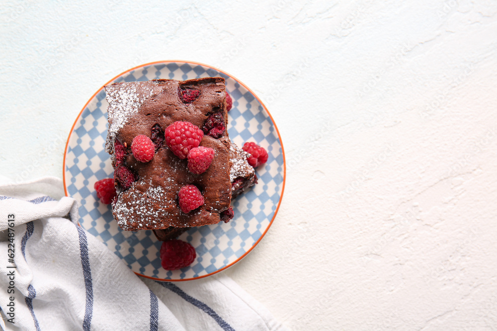 Plate with pieces of raspberry chocolate brownie on light blue table