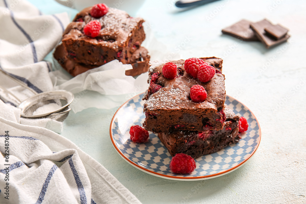 Baking paper and plate with pieces of raspberry chocolate brownie on light blue table