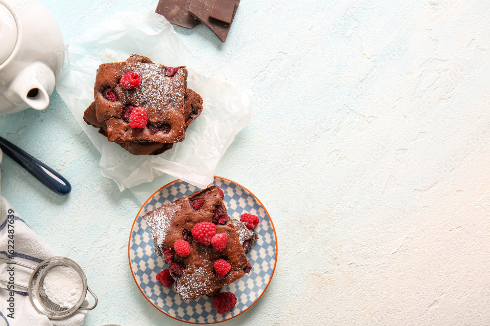 Baking paper and plate with pieces of raspberry chocolate brownie on light blue table