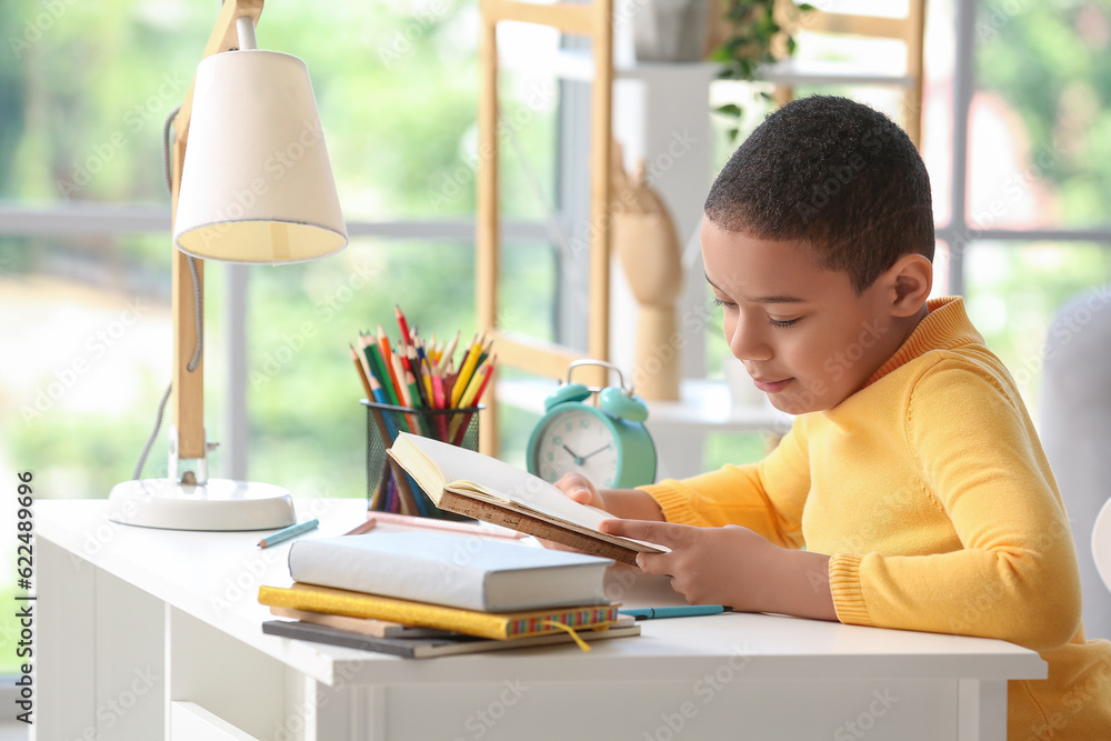 Little African-American boy reading schoolbook at home