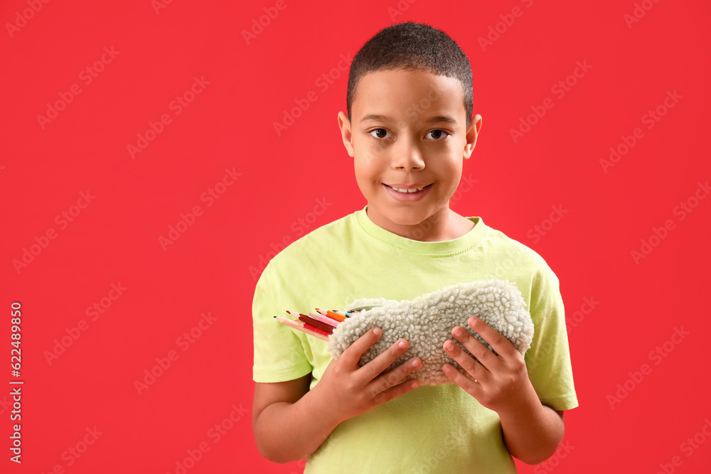 Little African-American boy with pencil case on red background