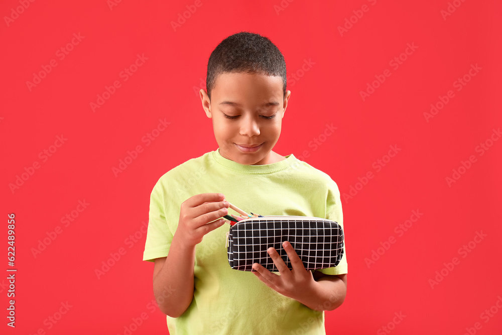 Little African-American boy with pencil case on red background