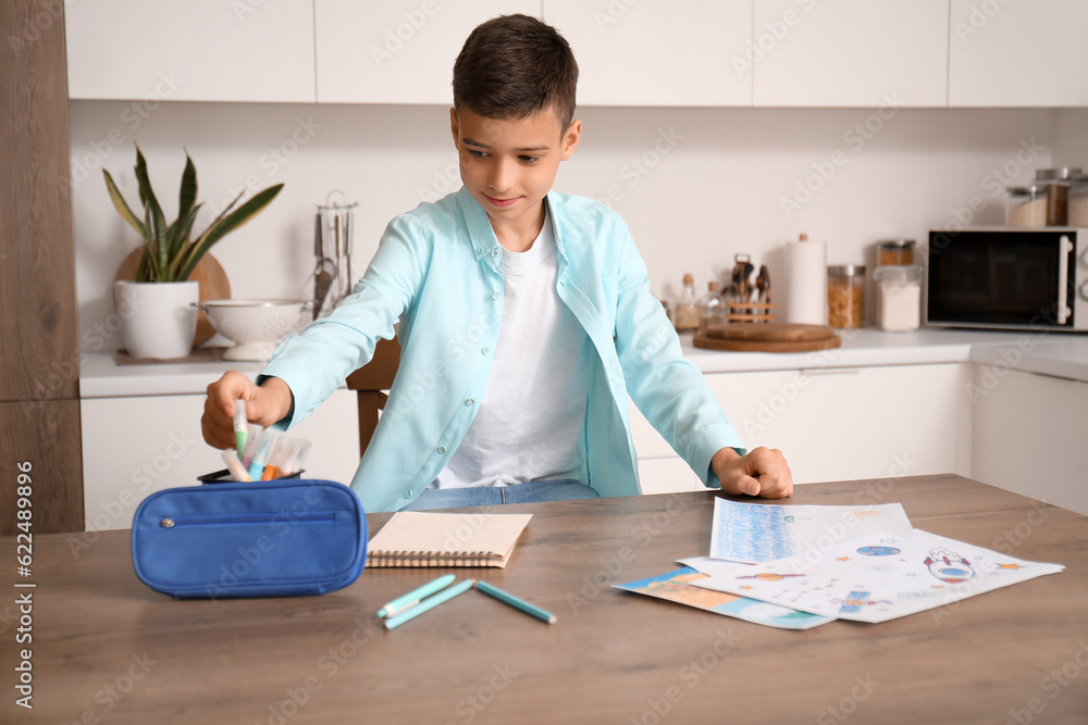 Little boy with pencil case at table in kitchen