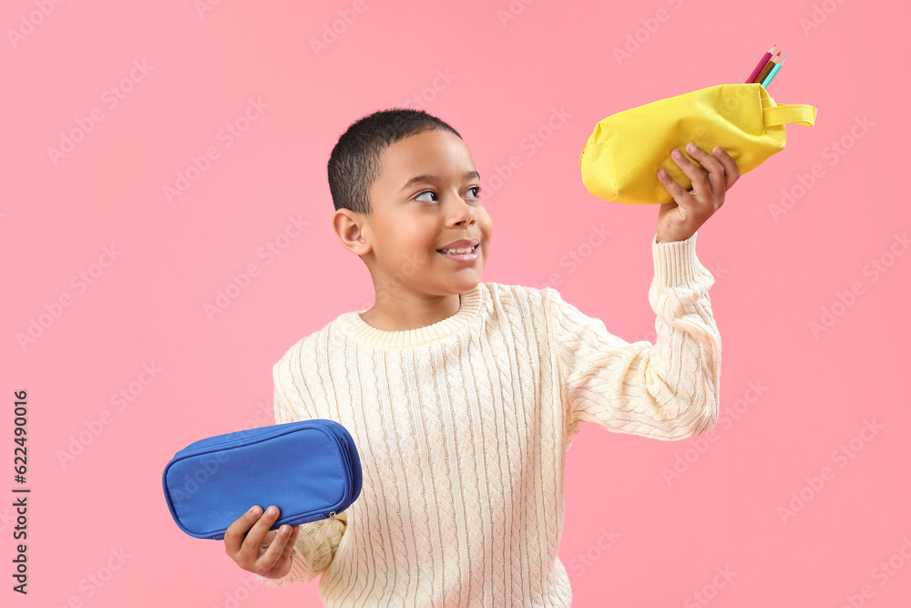 Little African-American boy with pencil cases on pink background