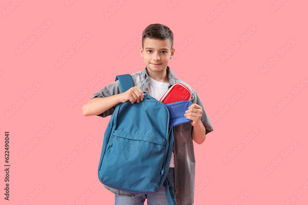 Little schoolboy with backpack and pencil cases on pink background