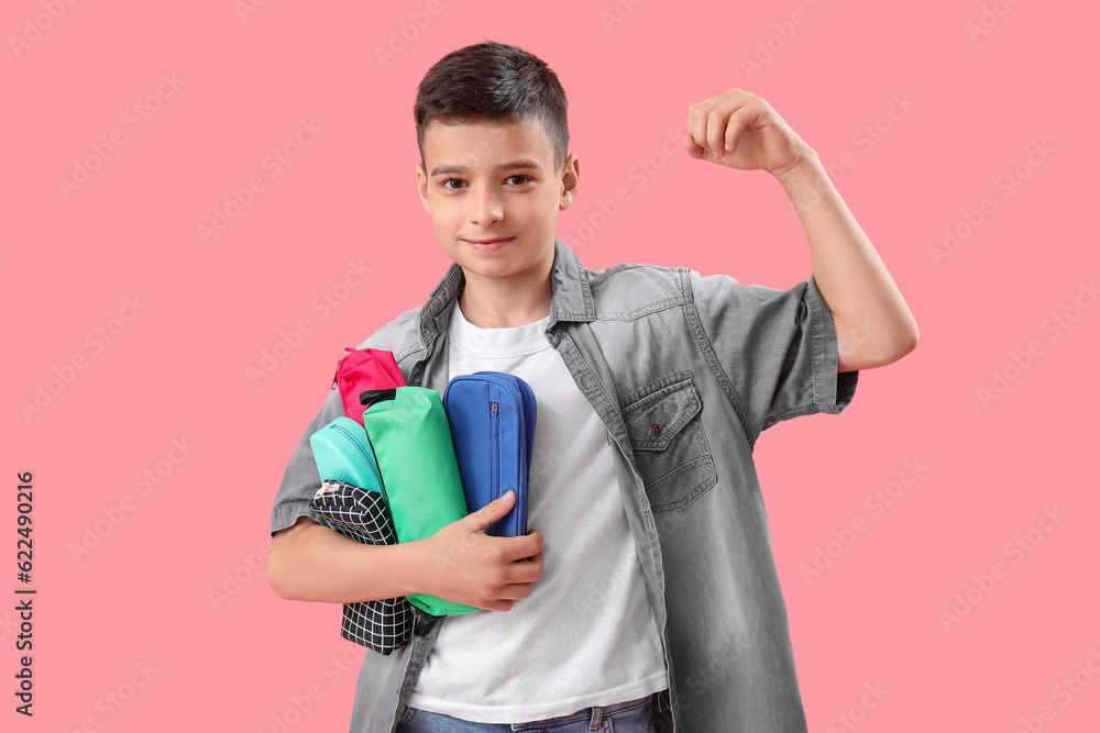 Little boy with pencil cases showing muscles on pink background