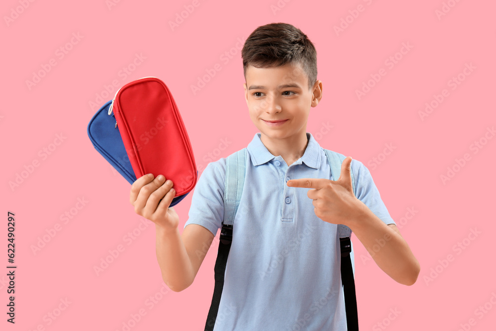 Little schoolboy pointing at pencil cases on pink background