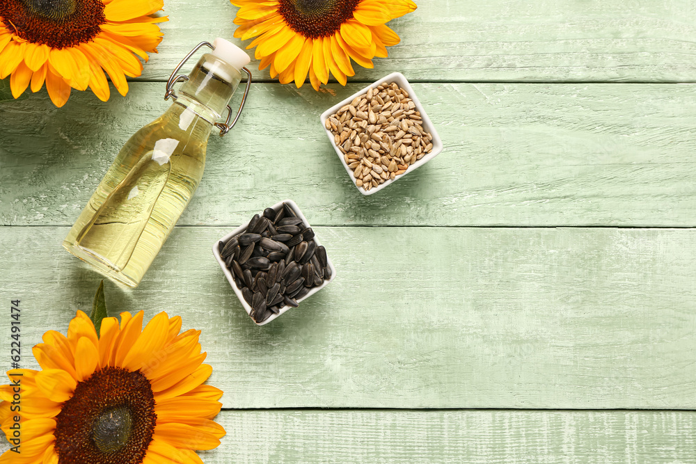 Sunflowers, bottle of oil and bowls with seeds on green wooden background