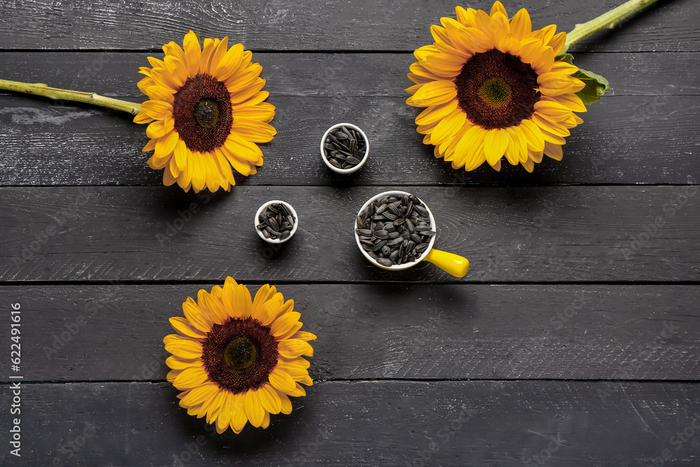 Sunflowers and bowls with seeds on black wooden background