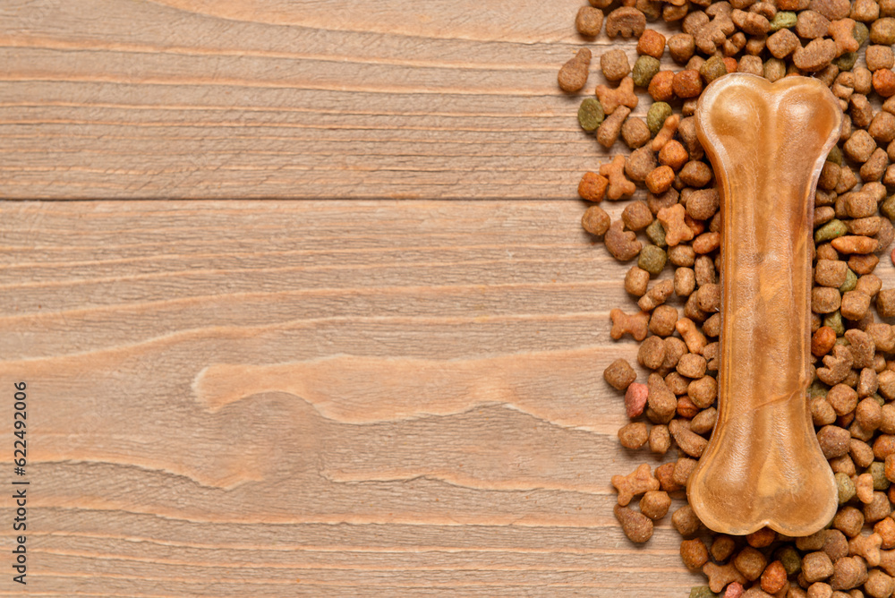 Heap of dry dog food and chew bone on wooden background