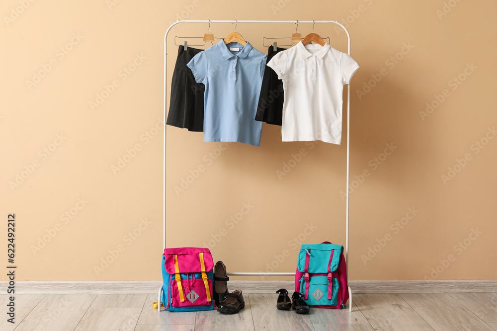 Rack with stylish school uniform, backpacks and shoes near color wall