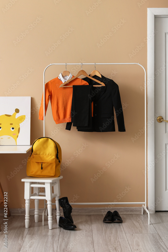 Rack with stylish school uniform, shoes and backpack near color wall in childrens room