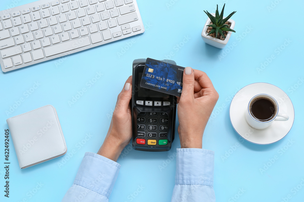 Female hands with credit card, payment terminal and cup of coffee on blue background