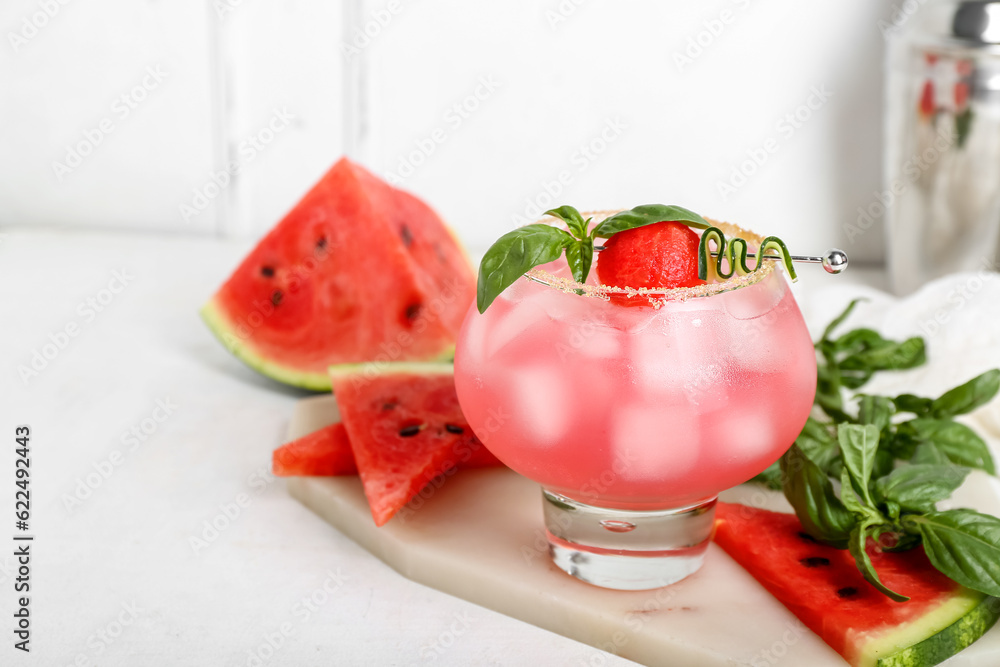 Board with glass of tasty watermelon cocktail, shaker and mint on white table