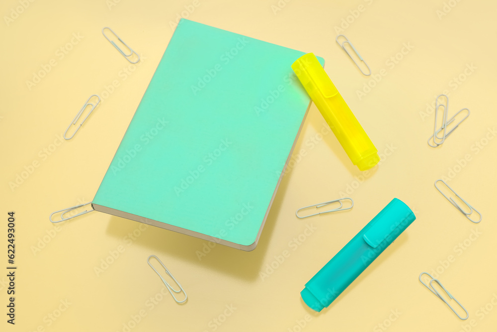 Notebook with different stationery on pale yellow background