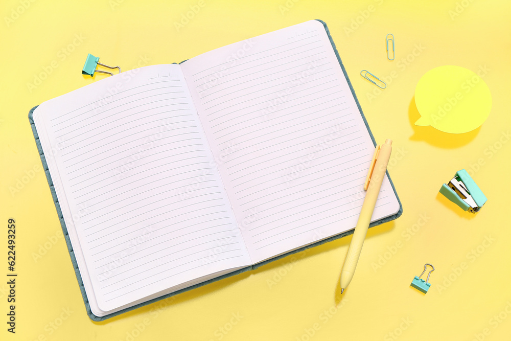 Blank notebook with stationery on yellow background