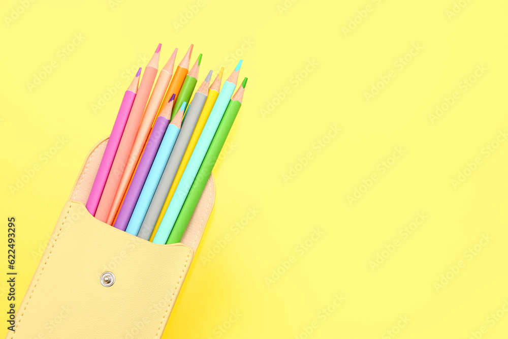 Different colorful pencils in case on yellow background