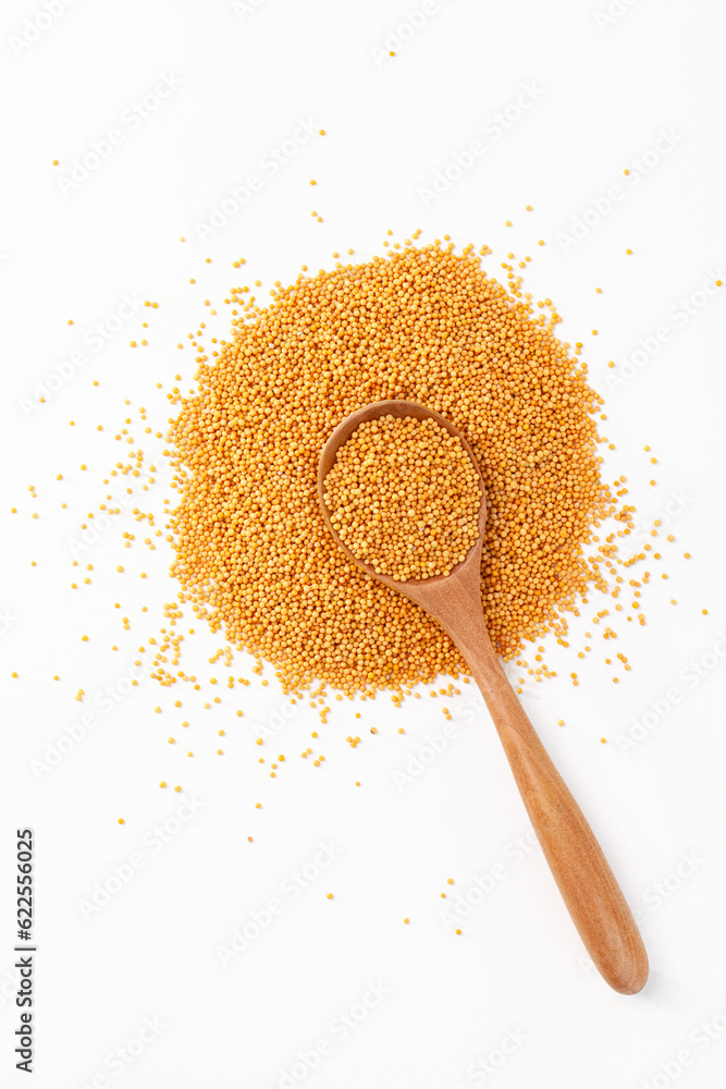 a pile of yellow mustard seeds with wooden spoon on white background. top view.