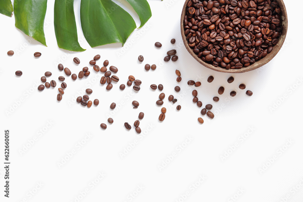 Roasted coffee beans in a coconut bowl and monstera leaf on a white background. Top view, flat lay. 