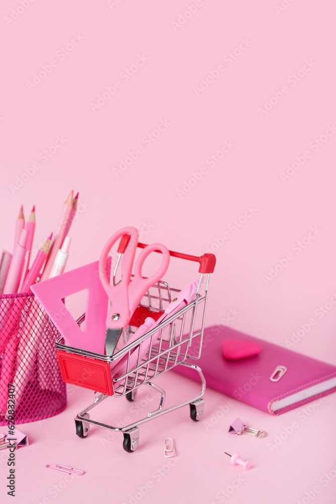 Shopping cart with stationery on pink background