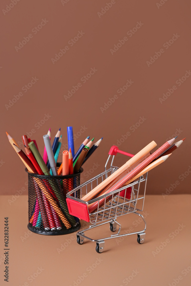 Shopping cart with pencils and felt-tip pens on color background