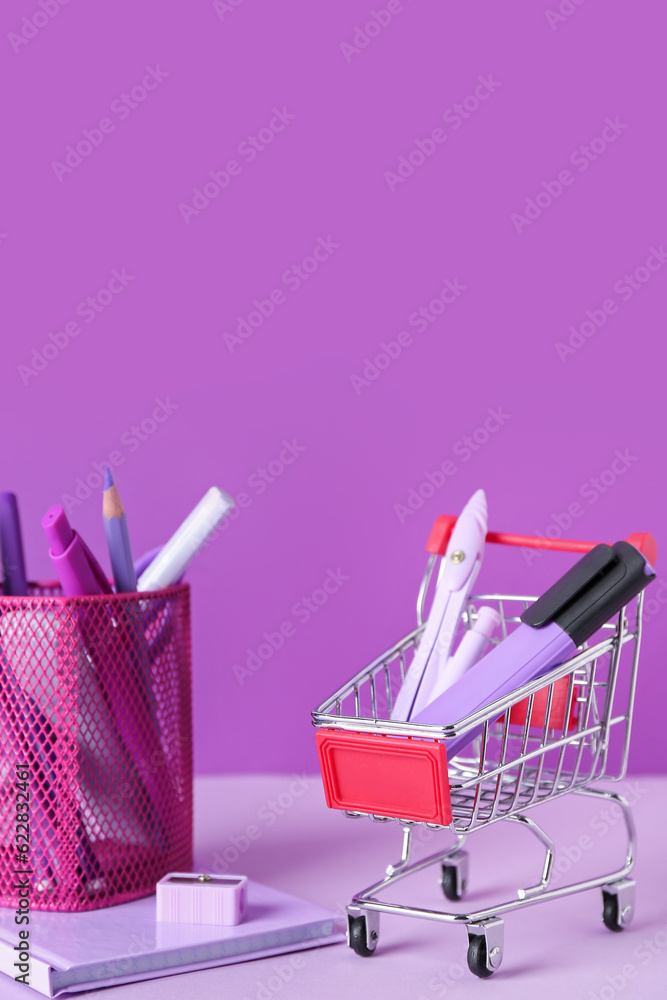 Shopping cart and holder with stationery on color background, closeup