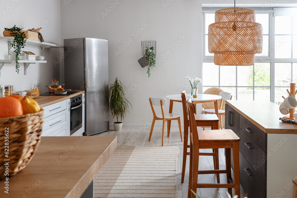 Interior of light kitchen with stylish fridge, counters, table and chairs