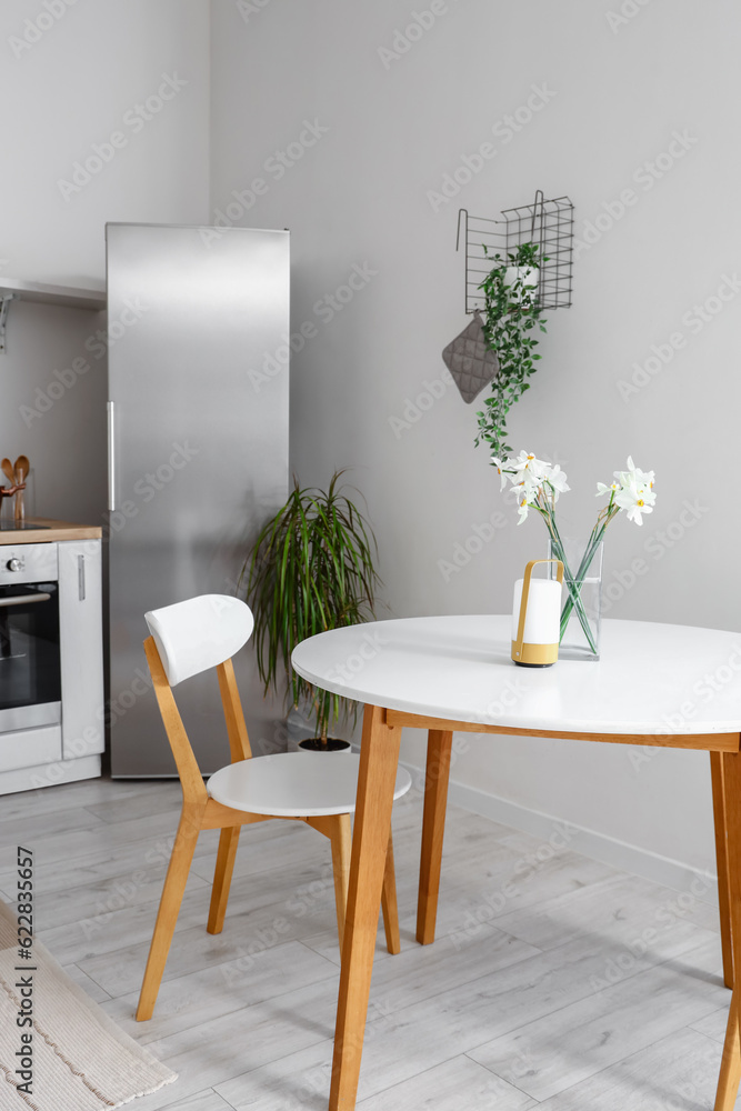 Vase with narcissus flowers and candle on table in interior of light kitchen