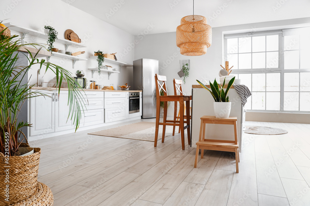 Interior of light kitchen with stylish fridge, counters, shelves and houseplants