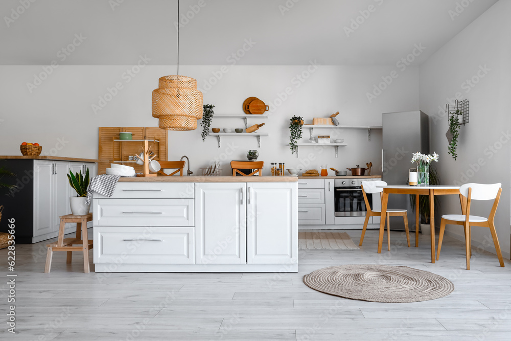 Interior of light kitchen with stylish fridge, counters, shelves, table and chairs