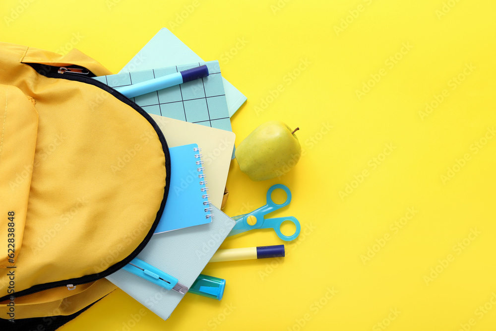 Color school backpack with apple, notebooks and markers on yellow background