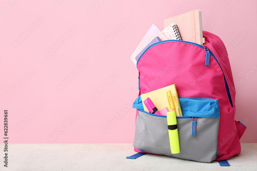 Pink school backpack with notebooks, pens and markers on white table near color wall