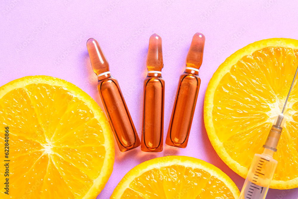 Ampoules with vitamin C, syringe and orange slices on purple background, closeup