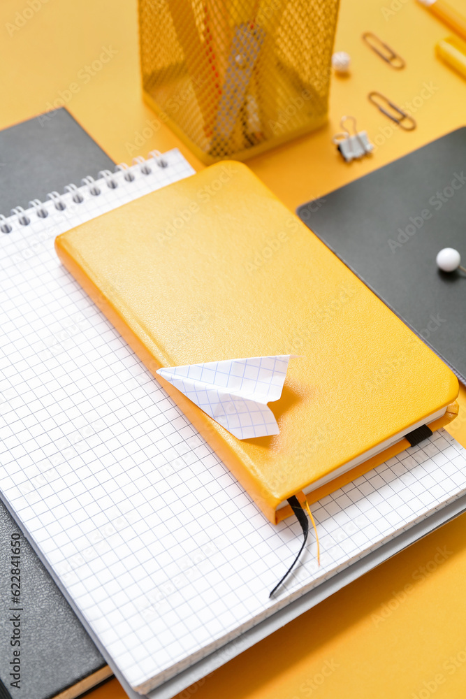 Notebooks, paper plane and different school stationery on orange background, closeup