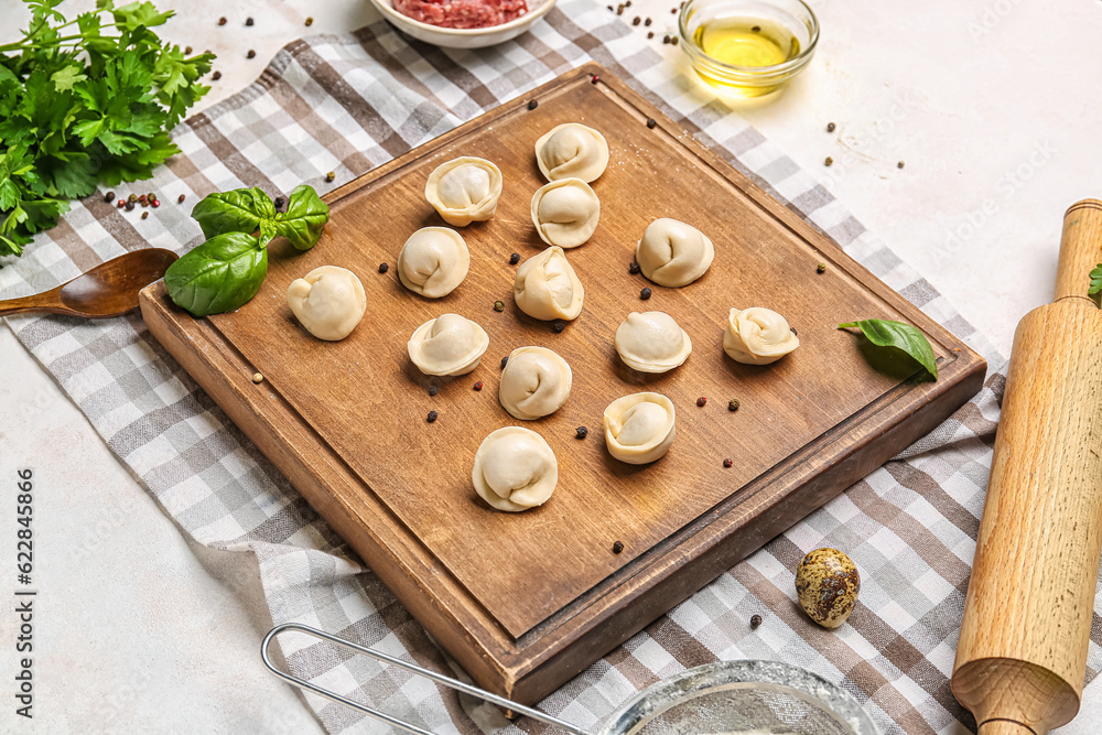 Board with uncooked dumplings on light background