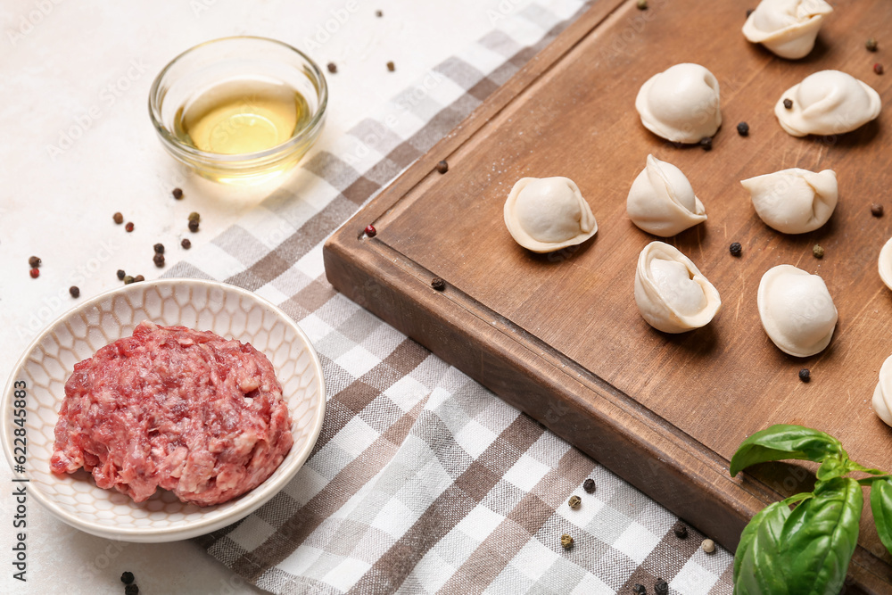 Board with uncooked dumplings and ingredients on light background