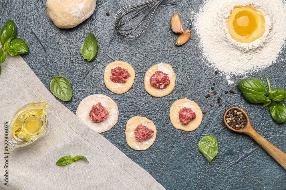 Raw dough with minced meat and ingredients for preparing dumplings on black background