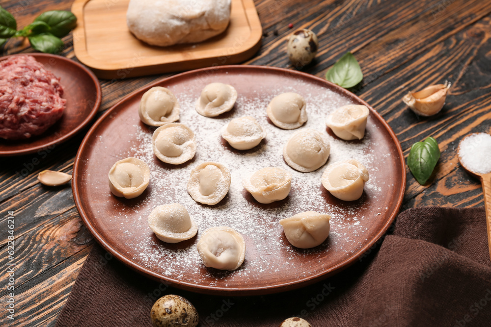 Plate with uncooked dumplings on wooden background