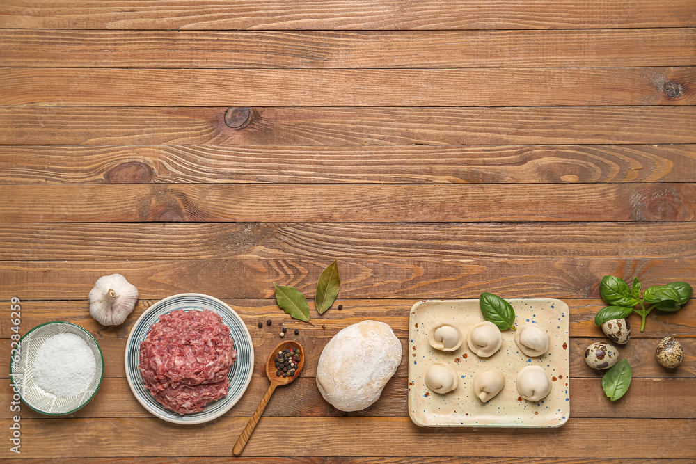 Plate with uncooked dumplings and ingredients on wooden background