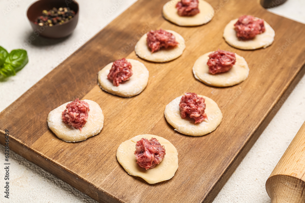 Wooden board of raw dough with minced meat for preparing dumplings on light background