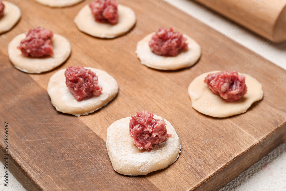 Wooden board of raw dough with minced meat for preparing dumplings on table