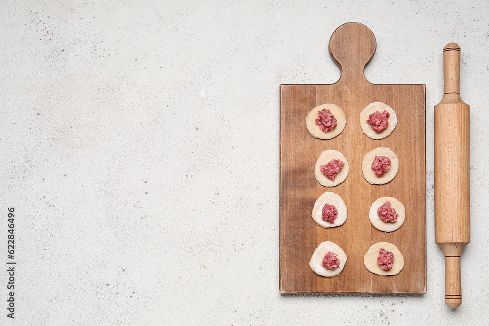 Wooden board of raw dough with minced meat for preparing dumplings on light background