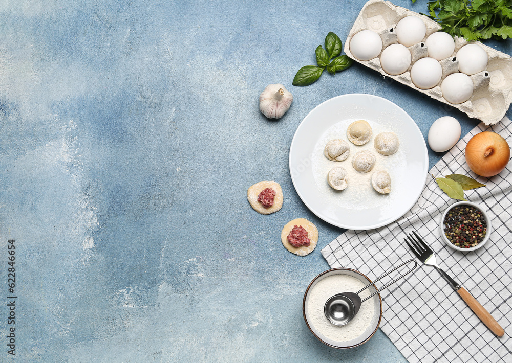 Plate with uncooked dumplings and ingredients on blue background